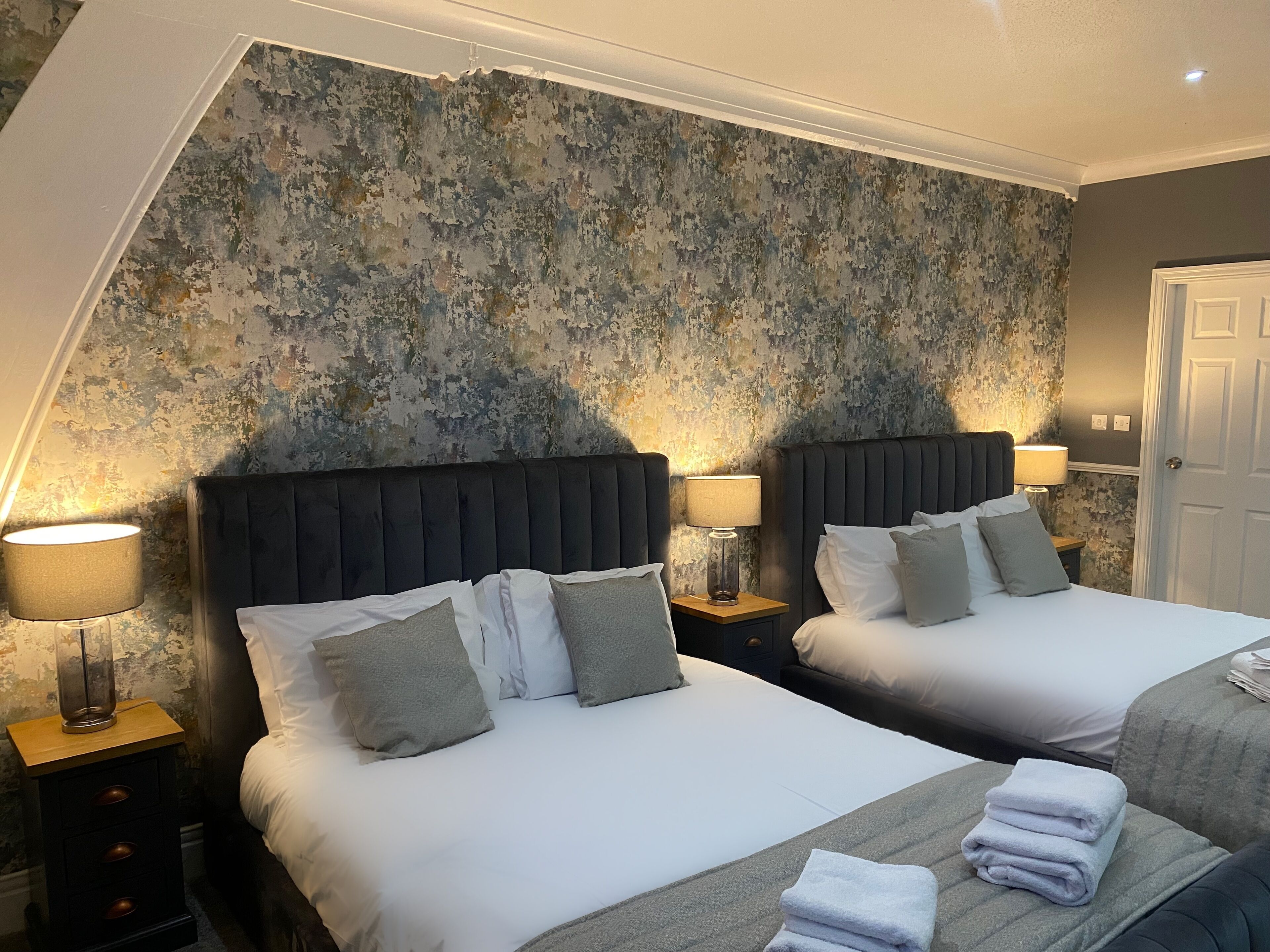 Habitación de hotel con dos camas, un ventanal grande y una pared con textura.
