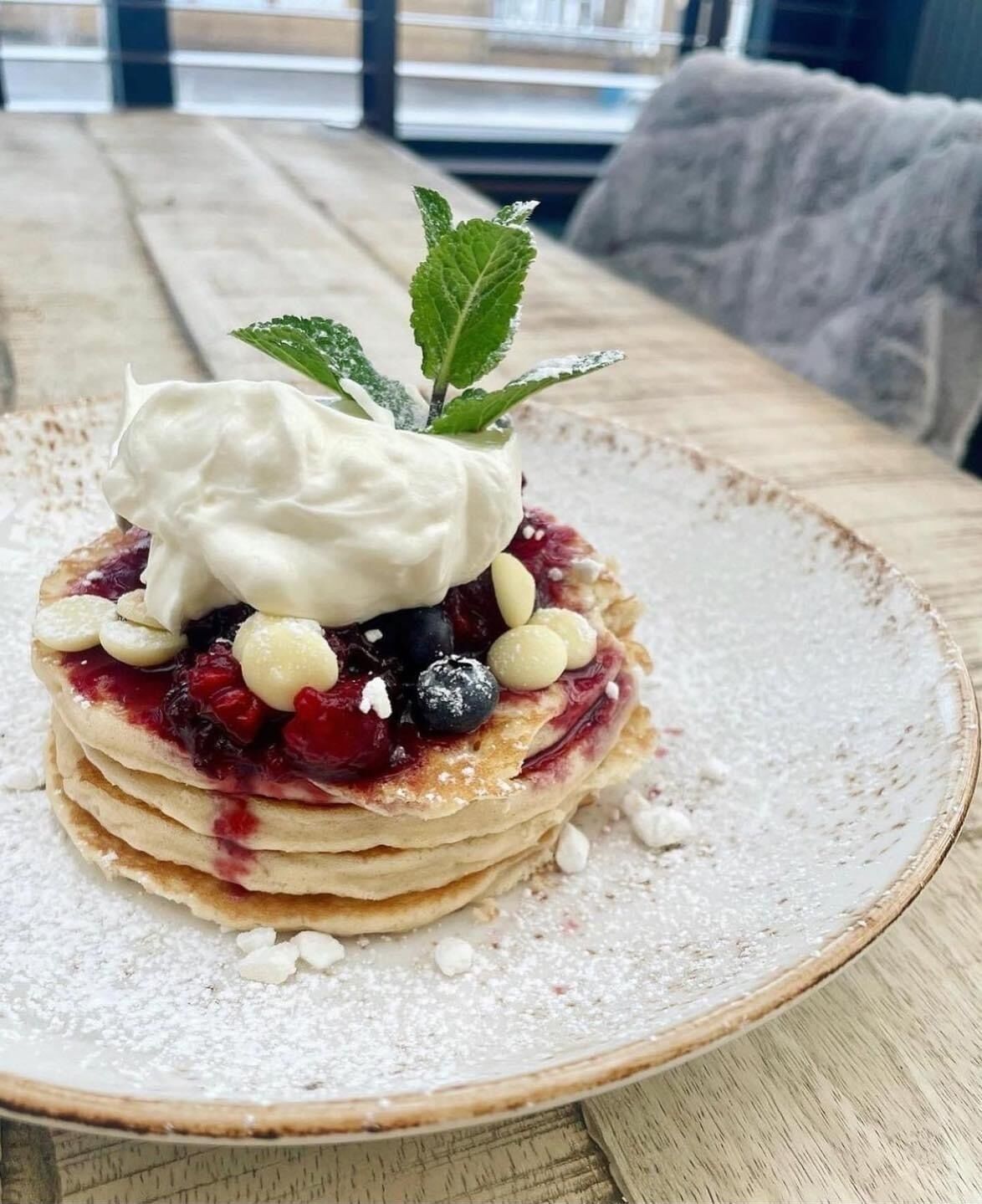 Ein Stapel Pfannkuchen mit Beeren und Schlagsahne auf einem Teller.
