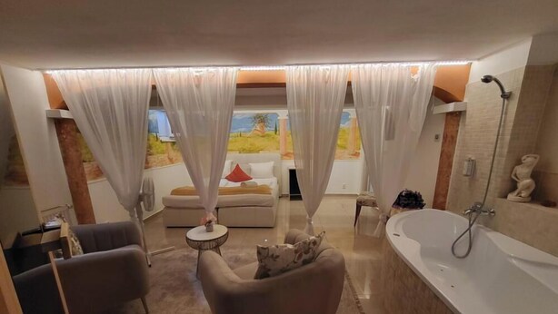 A modern bathroom with a large bathtub, a shower, and a sofa. - Penzion Janka (Brno)