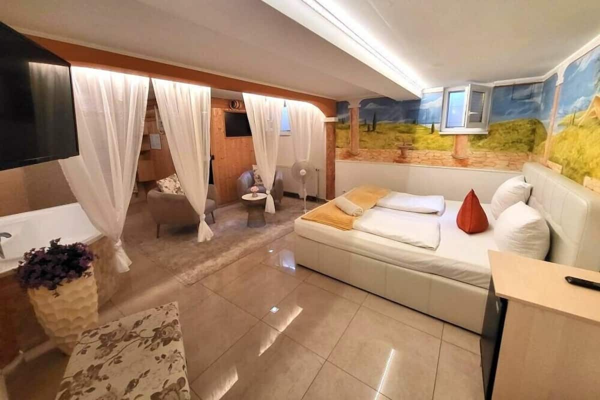 A modern hotel room with a bed, a sofa, a TV, a massage chair, and a large window with a scenic view.