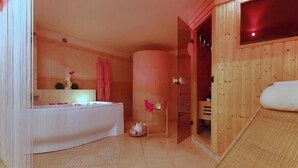 A wooden-finished room with a white bathtub, a small table with a basket, and a wicker chair. - Penzion Janka (Brno)