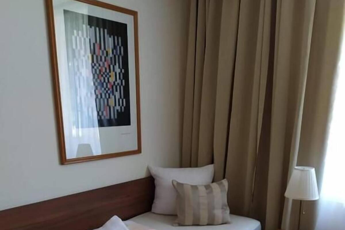 A neatly made bed with a red headboard, a bedside lamp, and a framed artwork on the wall.
