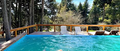 Une piscine avec une terrasse en bois et des chaises longues.