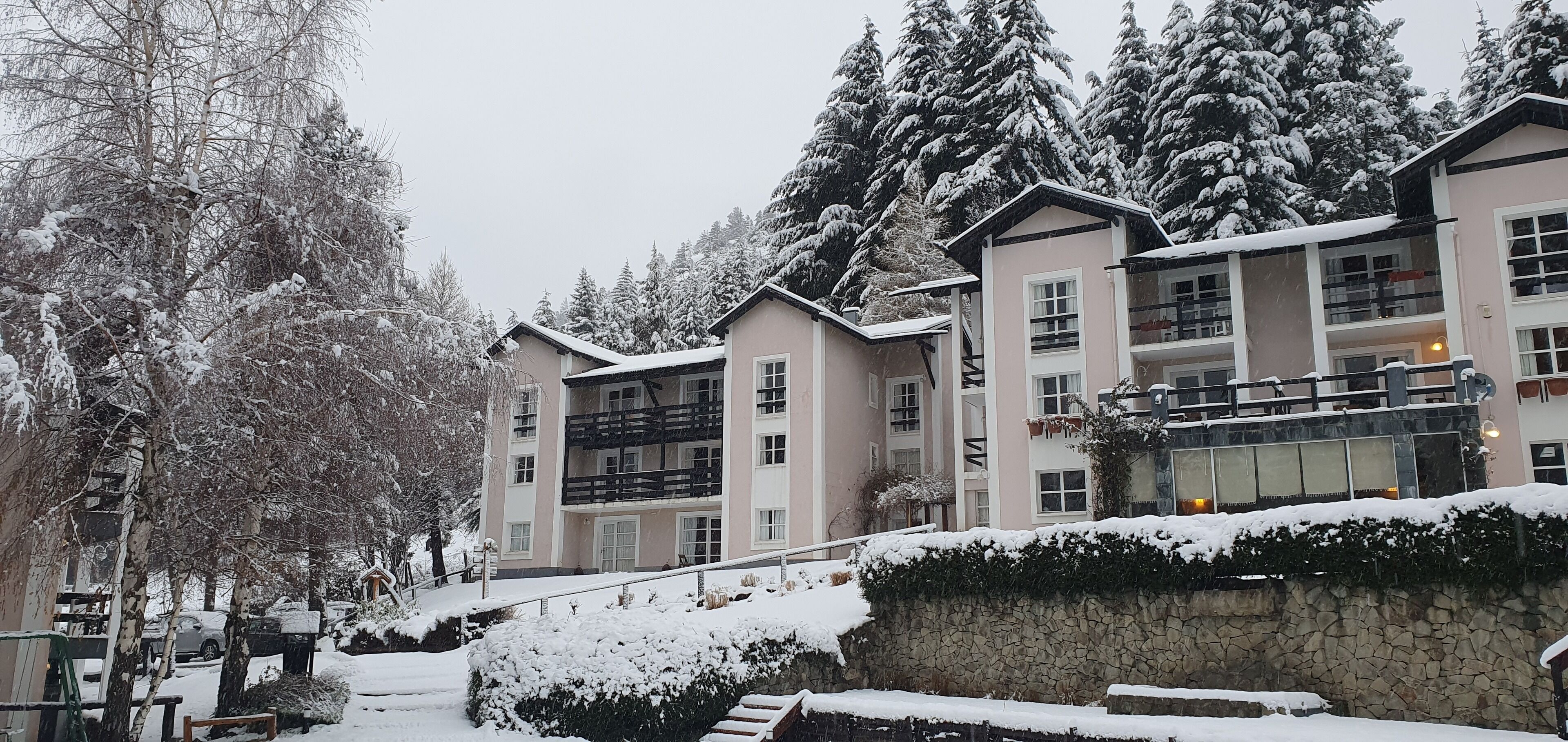 A multi-story hotel with a stone wall and snow-covered trees.