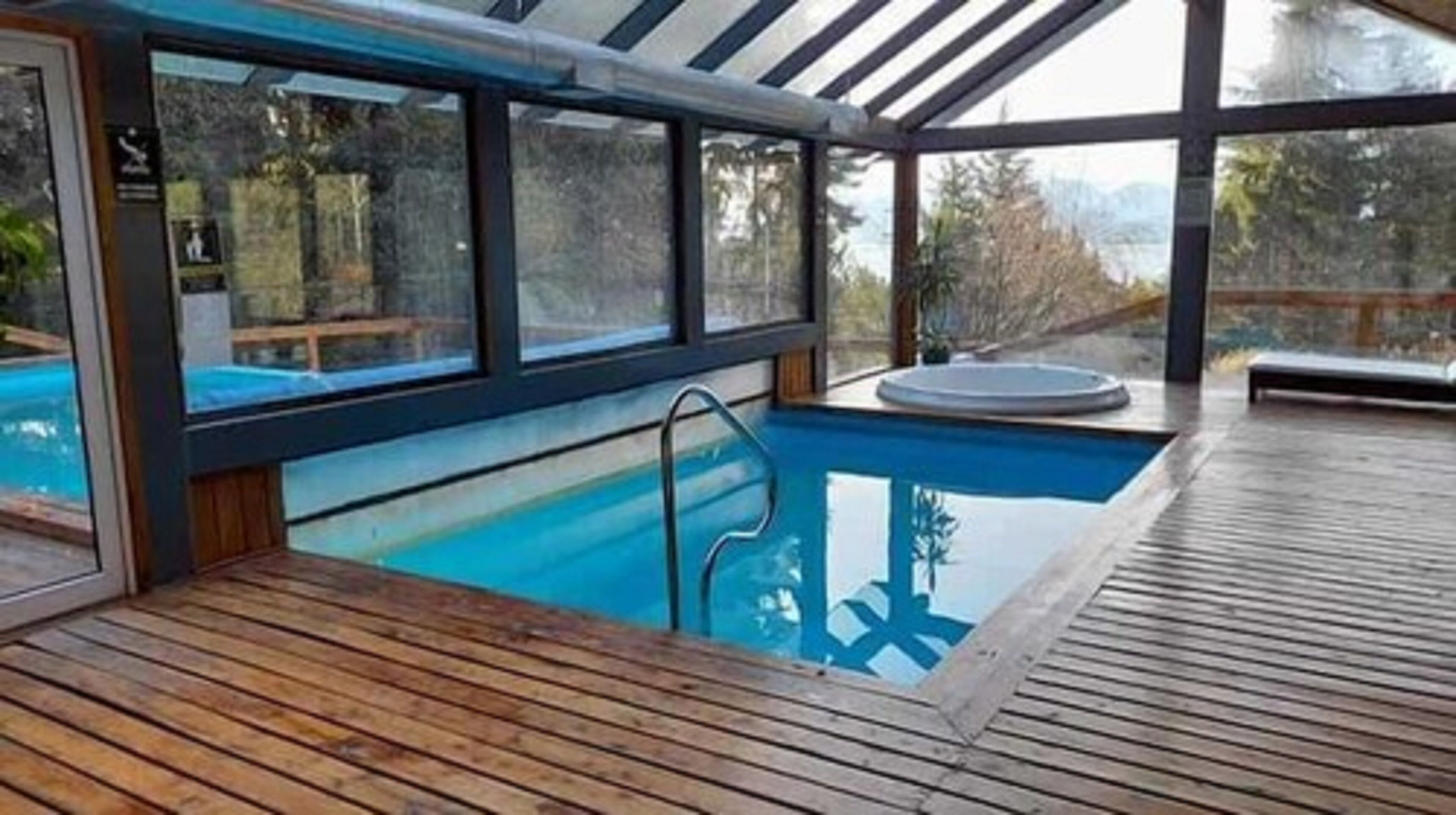 An indoor swimming pool with a wooden deck and glass walls.