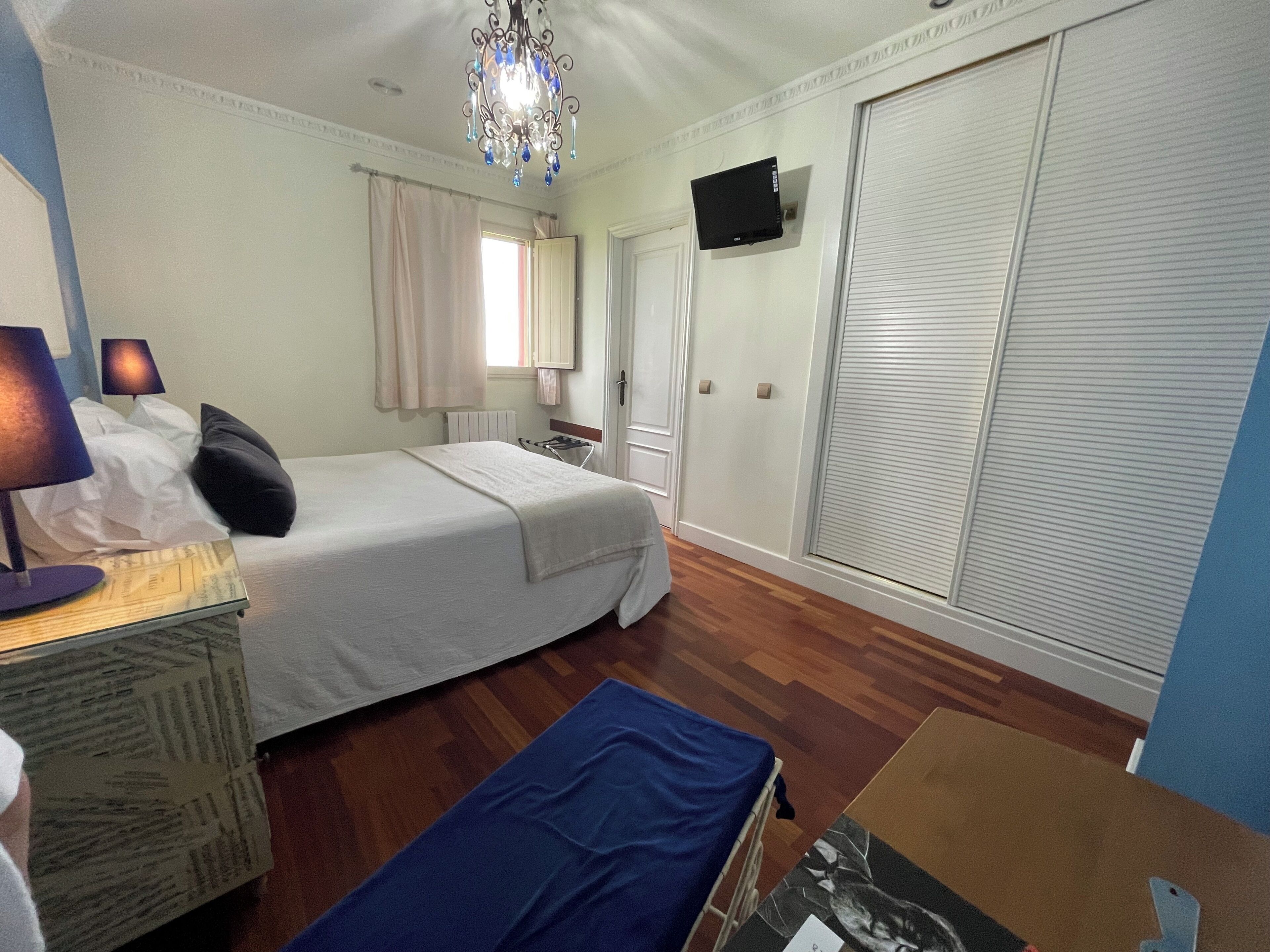Een slaapkamer met een bed, een bureau, een stoel, een televisie, een kledingkast en een kroonluchter.