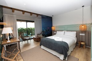 Ein Hotelzimmer mit Bett, Schreibtisch, Stuhl, kleinem Tisch und Blick ins Freie.
