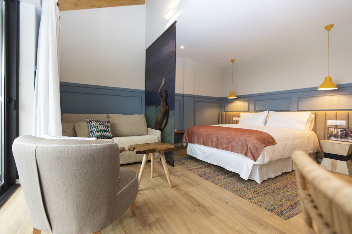Una habitación de hotel moderna con una cama grande, un sofá, una silla de madera y un cuadro en la pared.