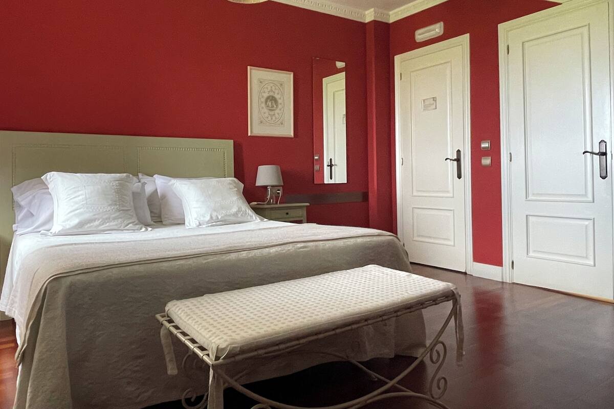 Una habitación de hotel con cama, mesita de noche, lámpara, banco y dos puertas.