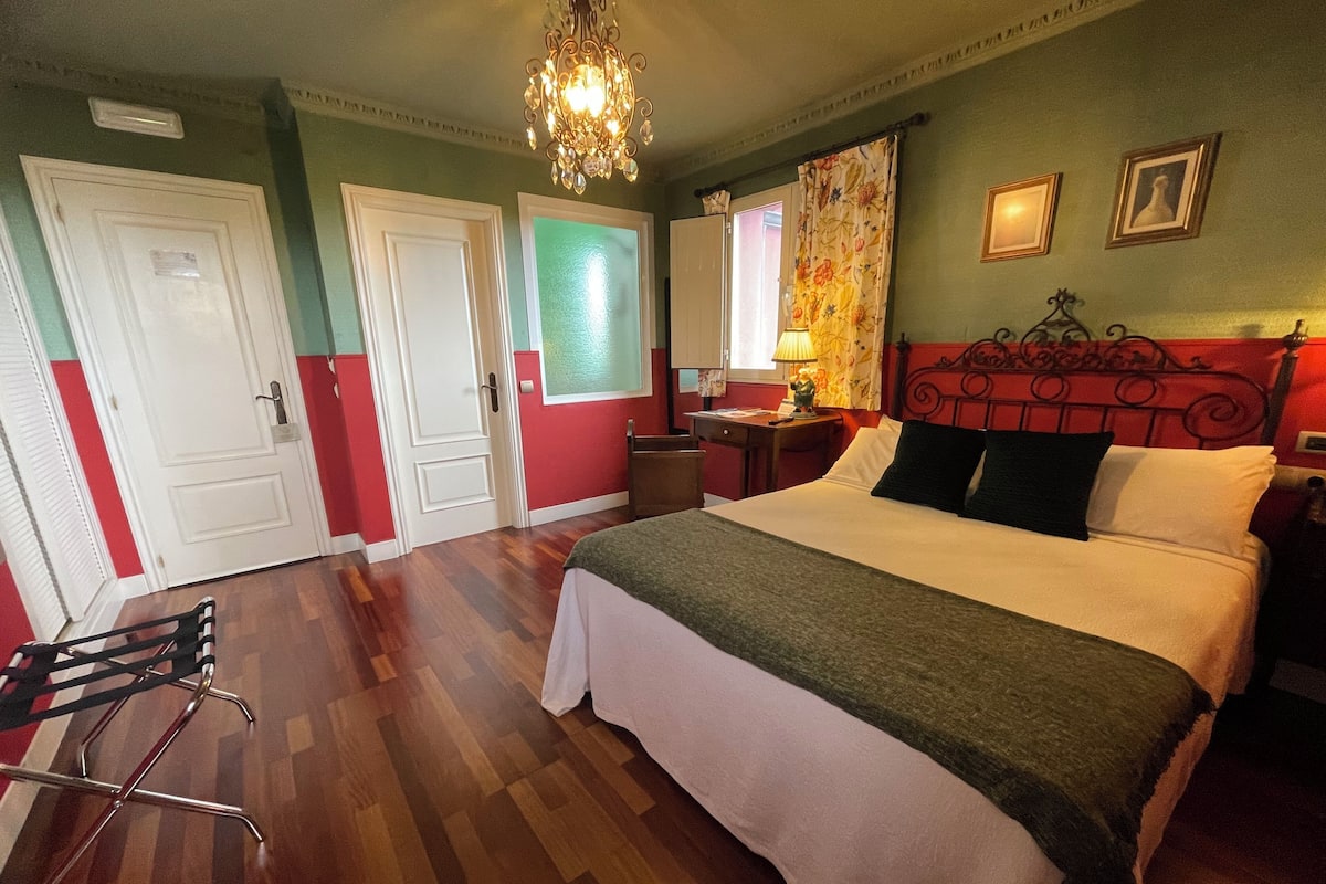 Una habitación de hotel con cama, escritorio, silla, lámpara y candelabro.
