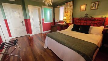 A hotel room with a bed, a desk, a chair, a lamp, and a chandelier.