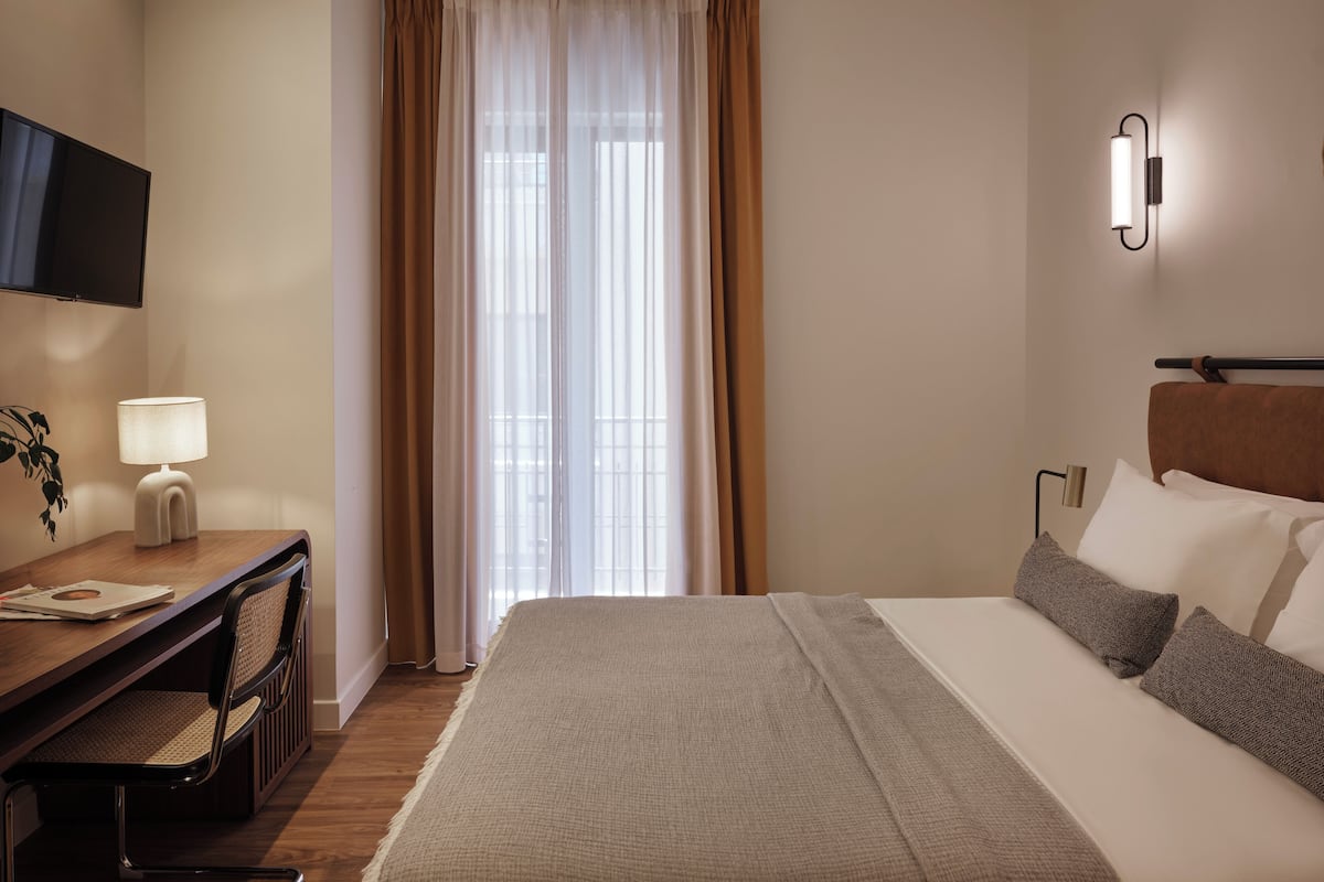 Une chambre d’hôtel avec un lit, un bureau avec une lampe, une chaise et un téléviseur fixé au mur.