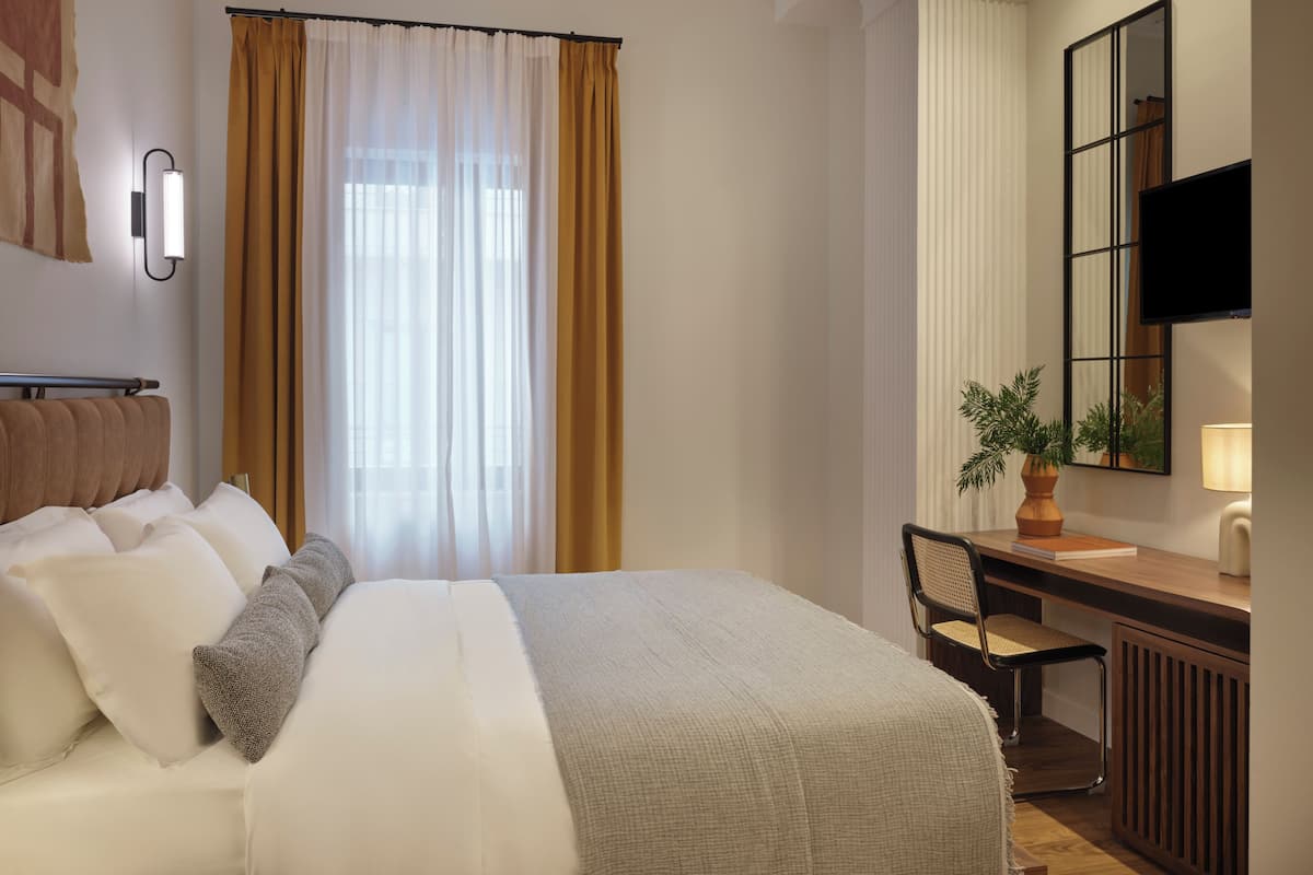 Une chambre d’hôtel avec un lit, un bureau, une chaise, un miroir et un téléviseur.