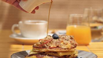 A breakfast setting with pancakes, blueberries, and syrup on a plate, with a cup and glass of orange juice in the background.