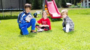 Three children sitting on grass in a park with playground equipment. - Cevedale (Valfurva)