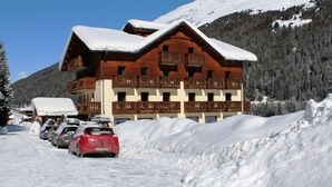 A wooden lodge with balconies, surrounded by snow-covered mountains and parked cars. - Cevedale (Valfurva)