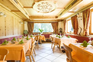 Ein Essbereich mit Holzwänden und -decke, Tischen mit grünen Servietten und einem Fenster mit Vorhängen.
