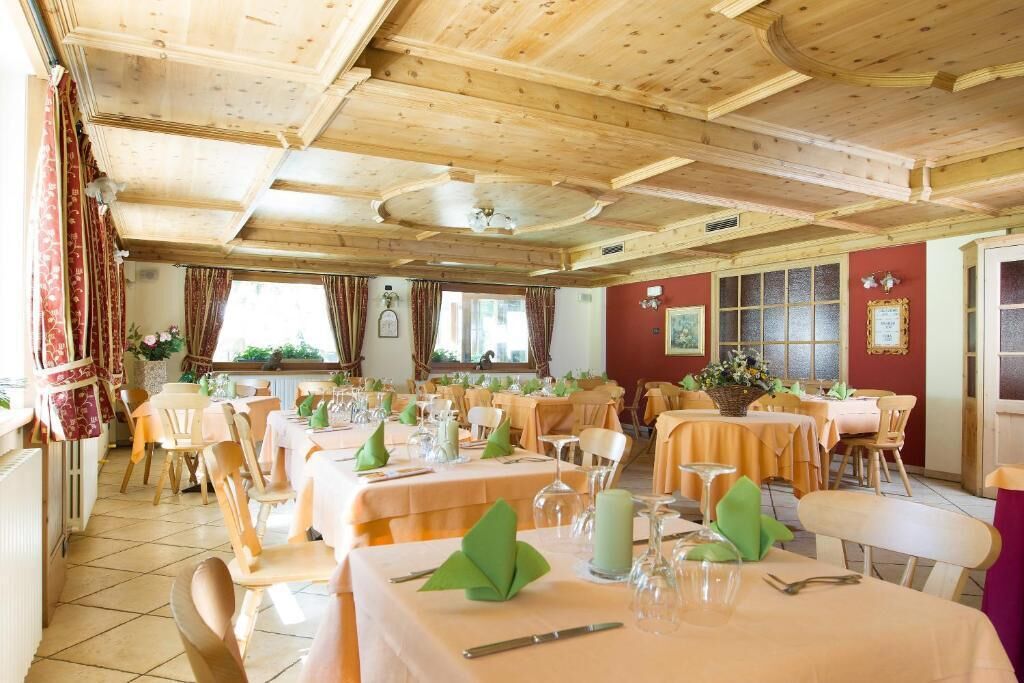 A dining area with multiple tables set for guests, wooden ceiling beams, and large windows allowing natural light.