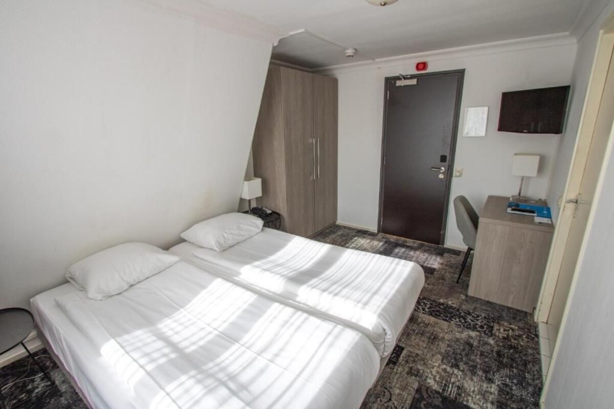 A hotel room with two beds, a desk, a chair, a wardrobe, and a door.