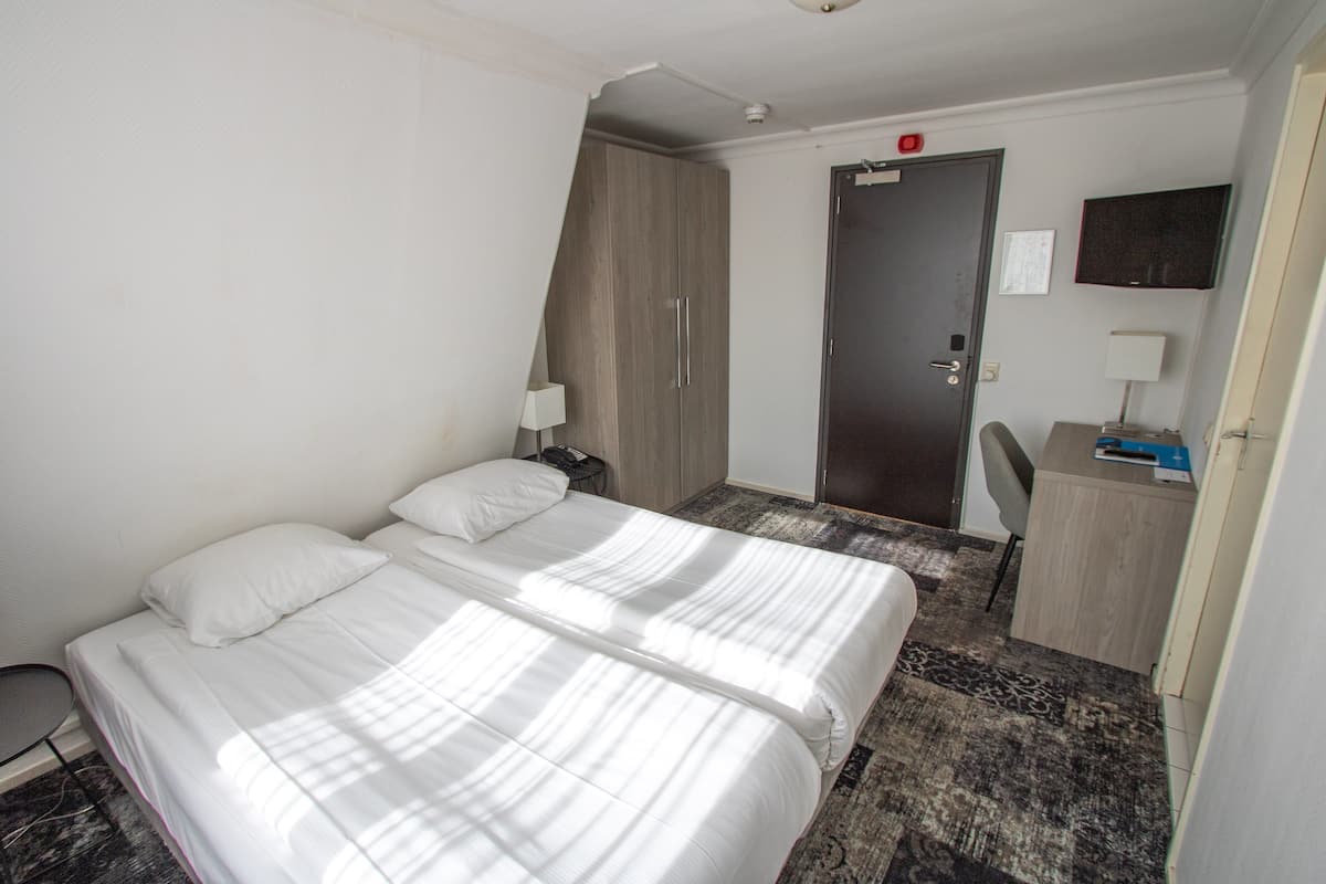 Hotellihuone, jossa on kaksi sänkyä, työpöytä, tuoli, lamppu ja vaatekaappi.