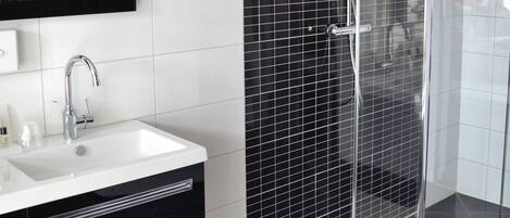 Une salle de bain moderne avec une douche à parois de verre, un lavabo blanc et un mur recouvert de carreaux noirs.