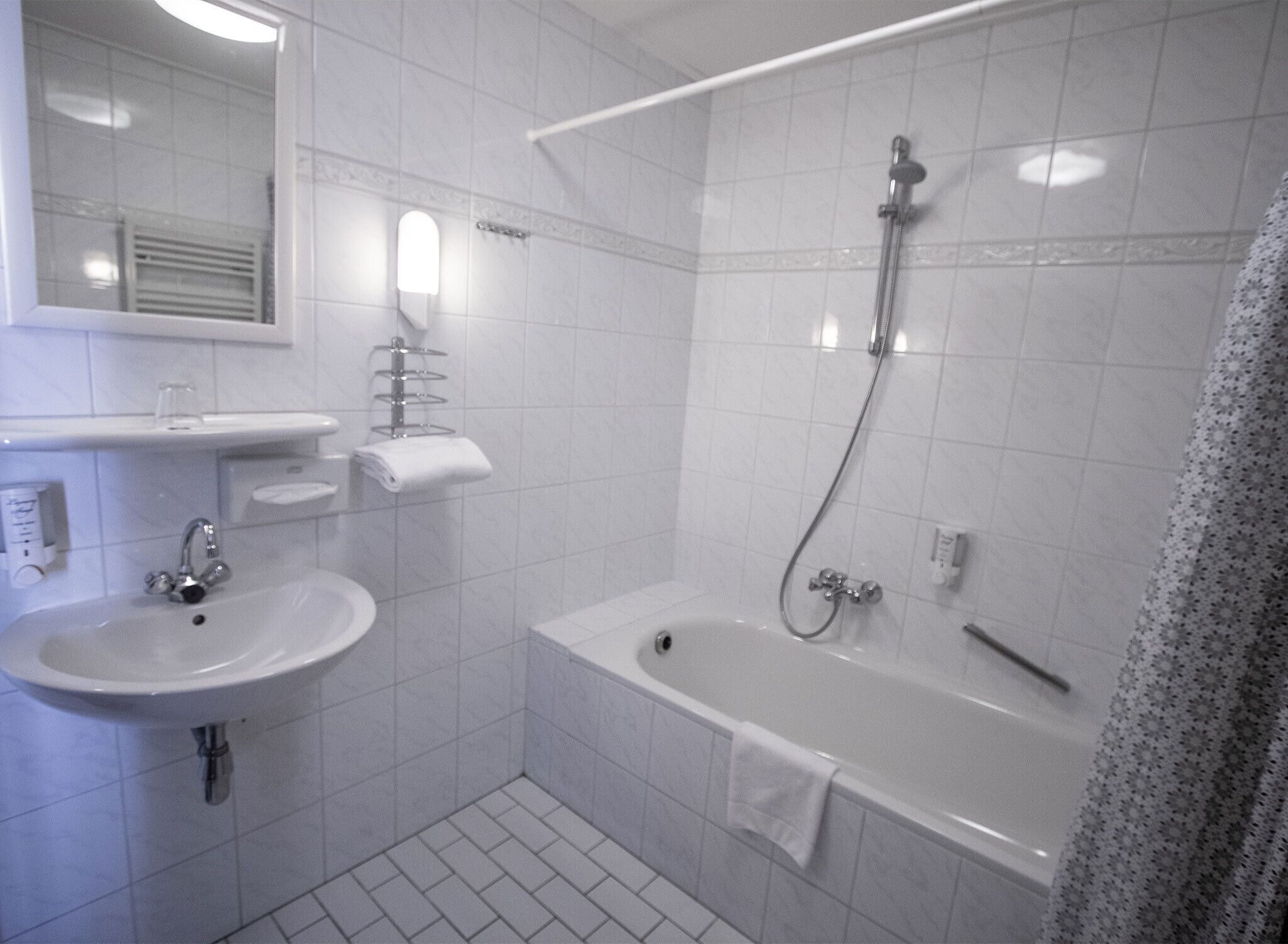 Un baño con lavamanos, espejo, toallero y zona de ducha.