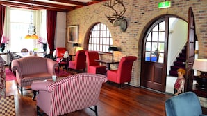 A lobby with striped red and white sofas, red chairs, a brick wall with a deer head mounted, and a staircase with a red carpet. - Fletcher Hotel Marijke (Bergen)