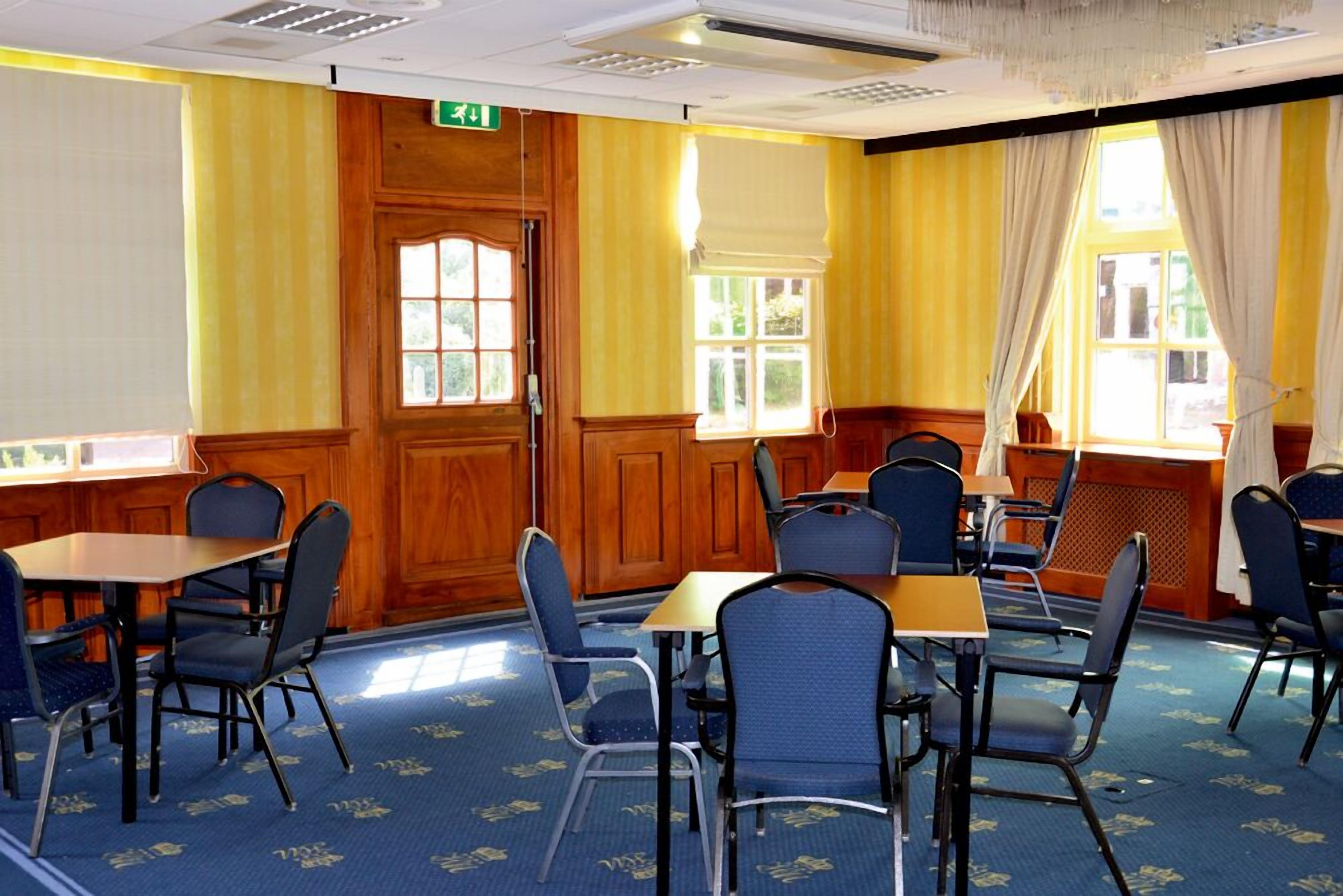 A conference room with wooden paneling, blue carpet, and tables with chairs.