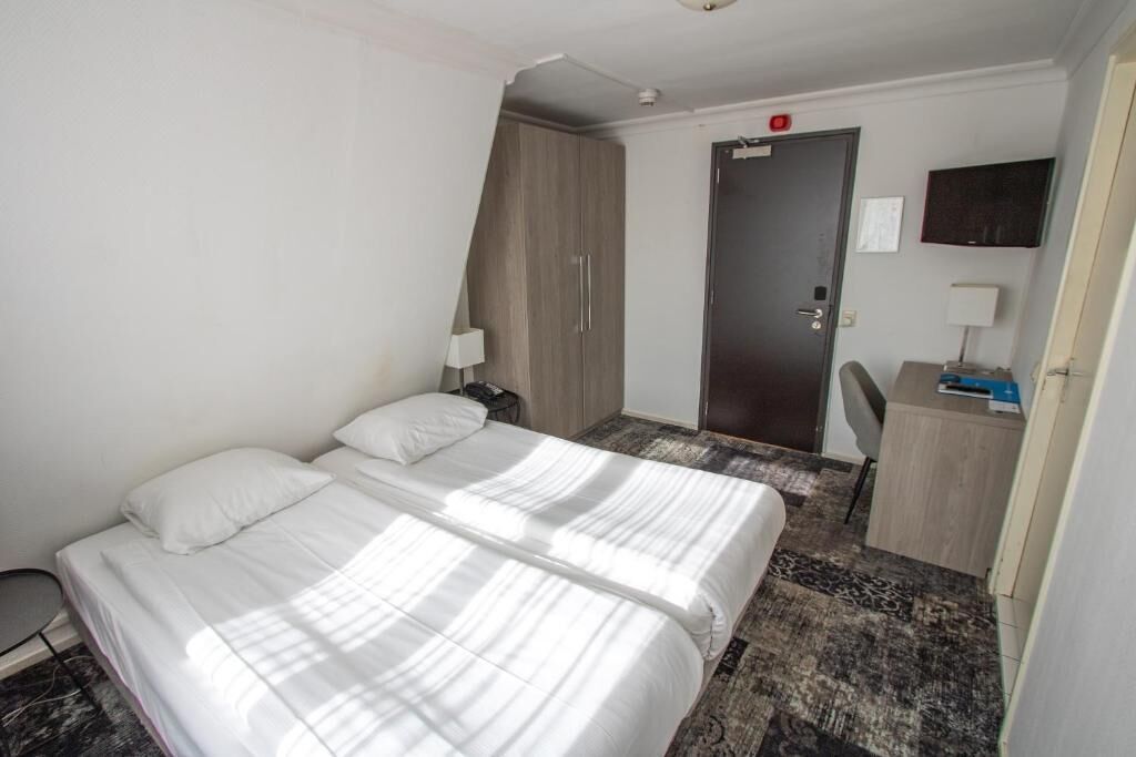 A hotel room with two beds, a desk, a chair, a wardrobe, and a door.
