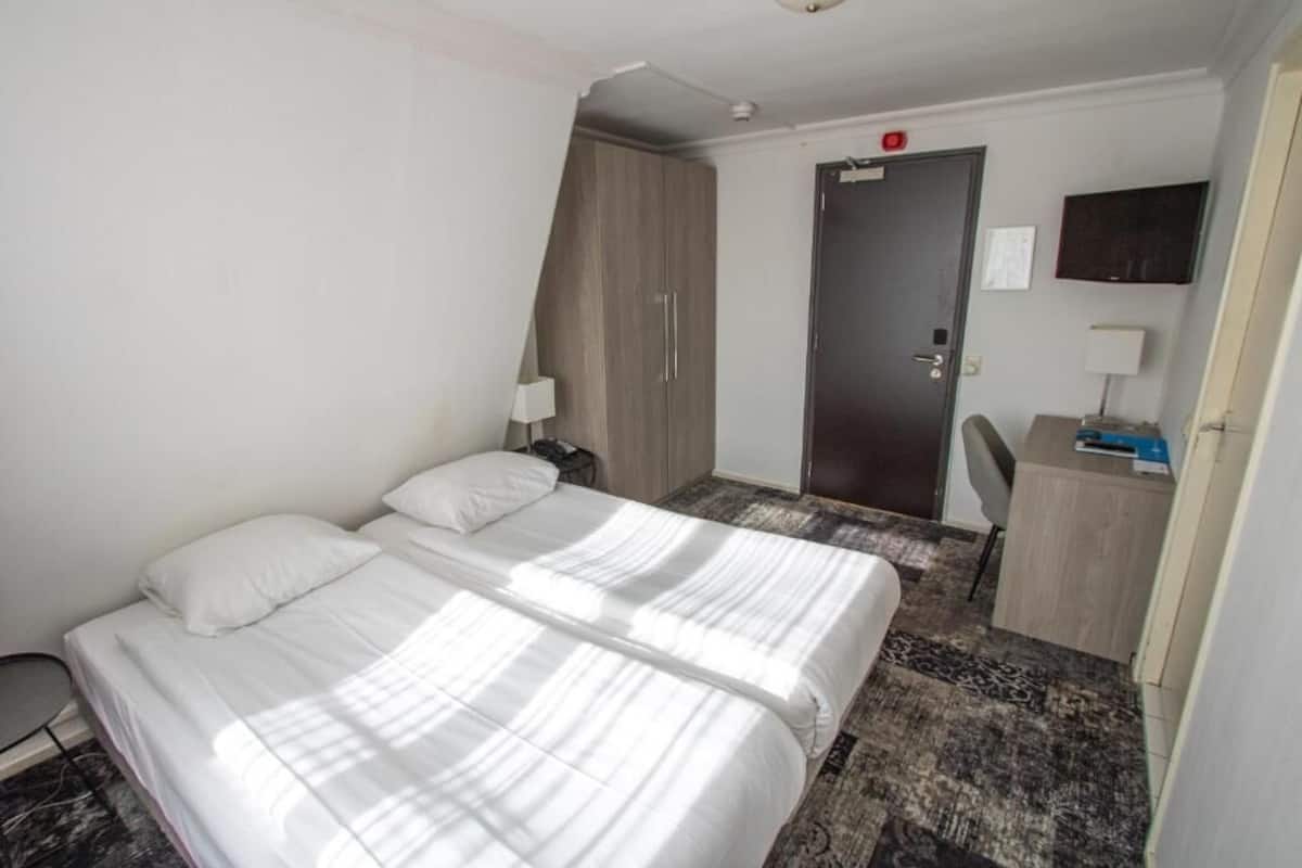 Hotellihuone, jossa on kaksi sänkyä, työpöytä, tuoli, vaatekaappi ja ovi.