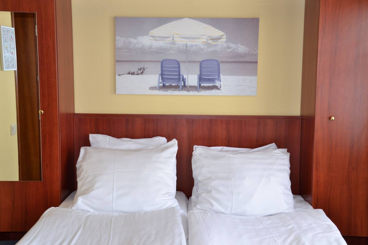 Hotellihuone, jossa on kaksi sänkyä, puinen pääty ja seinällä ranta-aiheinen taulu.