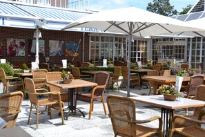 An outdoor cafe with wicker furniture and umbrellas. - Fletcher Hotel Marijke (Bergen)