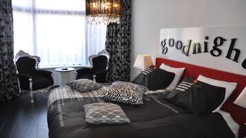 A hotel room with a bed, two chairs, a small table, and a chandelier.