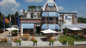 A hotel with a checkered awning, outdoor seating, and a garden area. - Fletcher Hotel Marijke (Bergen)