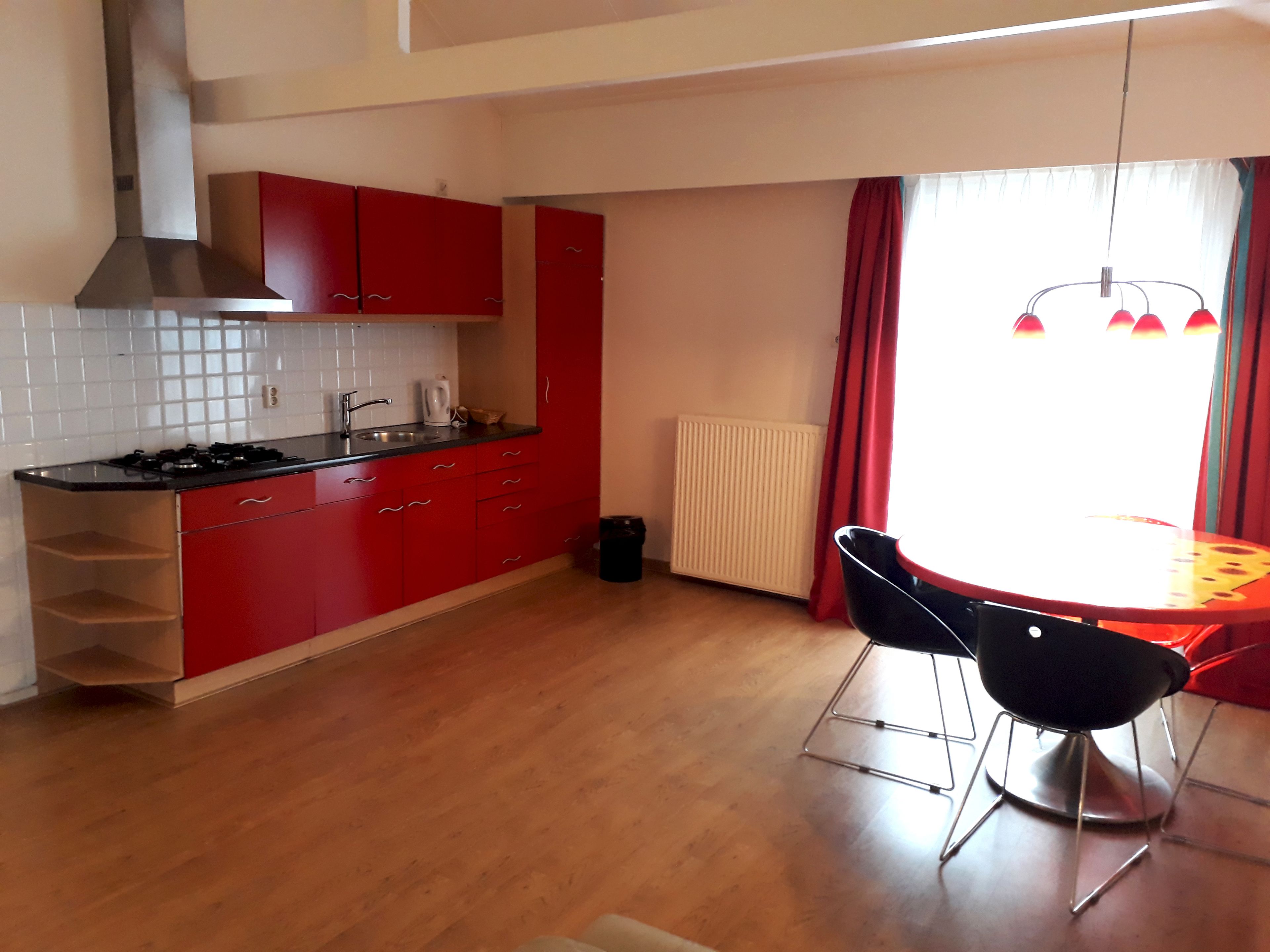 Una cocina compacta con armarios rojos, una estufa a gas y un pequeño comedor con una mesa y dos sillas.