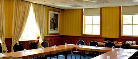 Un salón de conferencias con largas mesas, sillas y una araña.