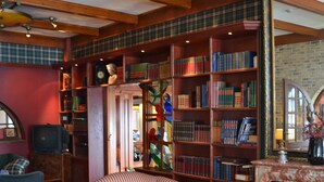 A cozy living room with a fireplace, striped armchairs, a coffee table, and a bookshelf filled with books. - Fletcher Hotel Marijke (Bergen)