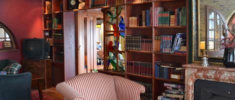 Una sala de estar acogedora con chimenea, sillones a rayas, una mesa de centro y una estantería llena de libros.