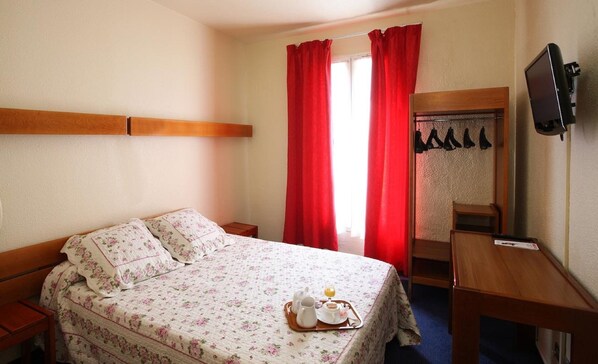 Hotellihuone, jossa on sänky, yöpöytä, työpöytä, tuoli, peili ja televisio.