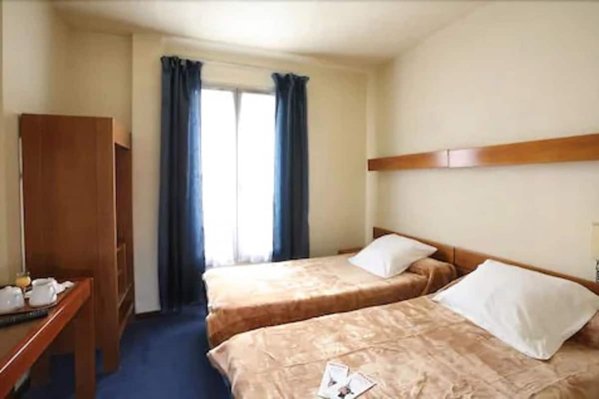 A hotel room with two beds, a wooden desk, and a window with curtains.