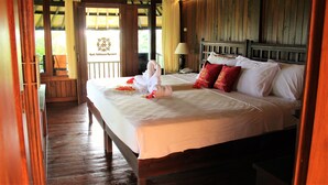 A hotel room with a bed, pillows, a lamp, and a view of the outdoors. - Bali Nibbana Resort (Seririt)