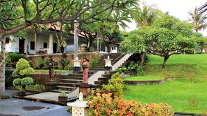 A traditional building with a staircase leading to a porch, surrounded by lush greenery and potted plants. - Bali Nibbana Resort (Seririt)