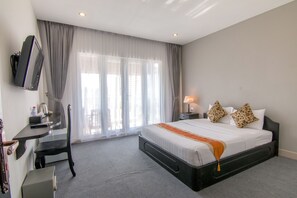 A hotel room with a bed, a desk, a chair, a TV, and a window with curtains.