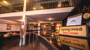 A hotel lobby with a reception desk, a decorative cat statue, and a sign with 'WELCOME' in multiple languages. - Diamond Palace Hotel (Phnom Penh)