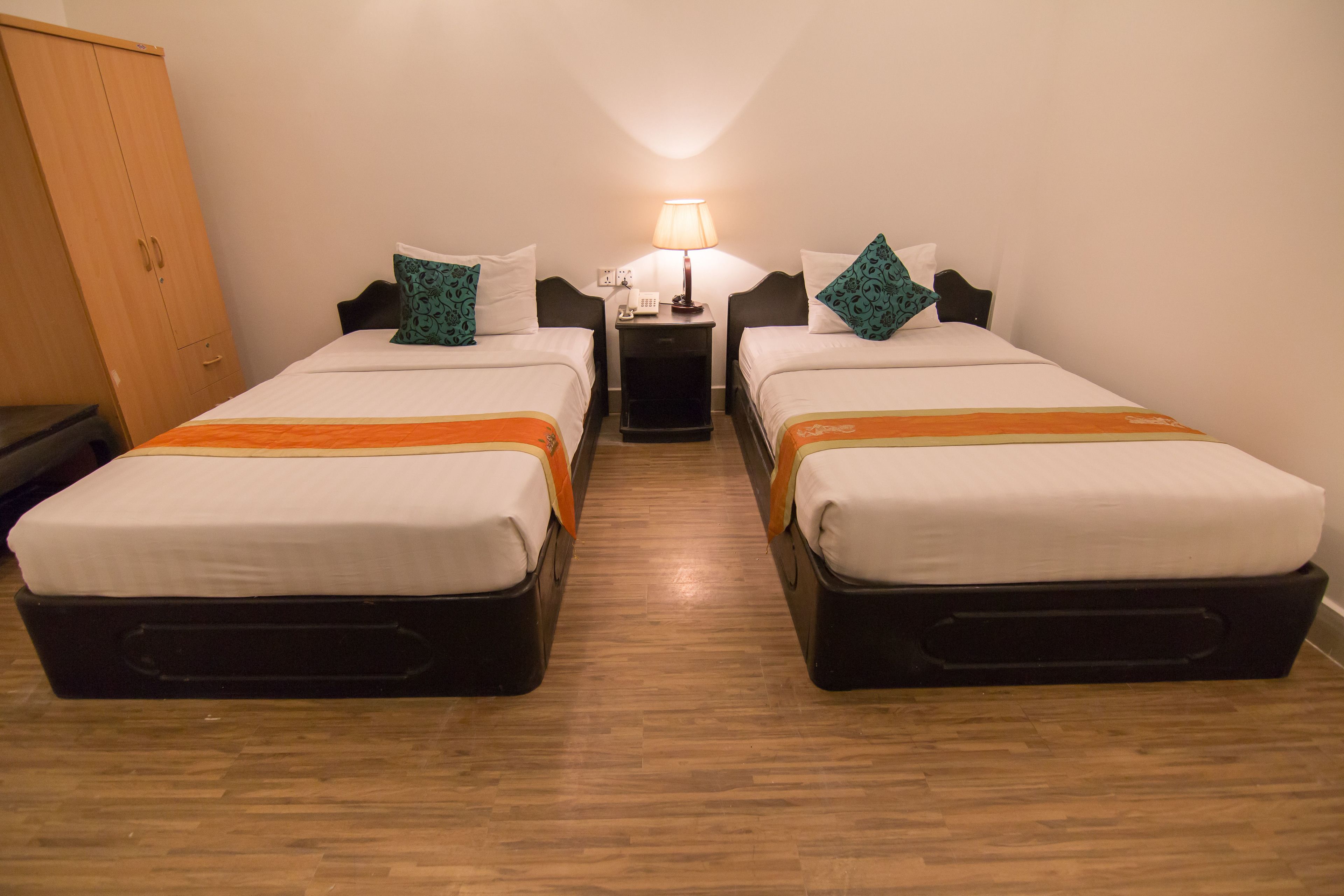 A hotel room with two single beds, a wooden wardrobe, a nightstand with a lamp, and a telephone.