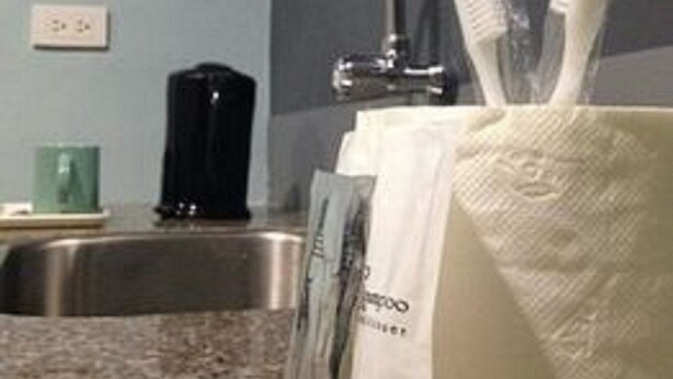 A bathroom with a sink, a mirror, a faucet, a soap dish, and a bag of toiletries. - Leesons Residences (Manila)