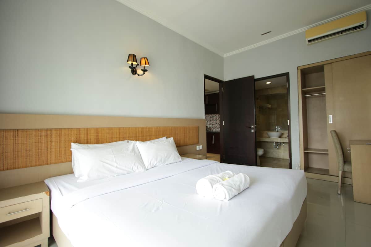 A hotel room with a large bed, a nightstand, a wardrobe, and a bathroom visible through an open door.