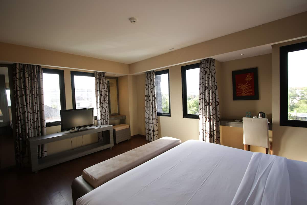 A hotel room with a bed, a TV on a desk, a desk chair, a computer, and a window with curtains.