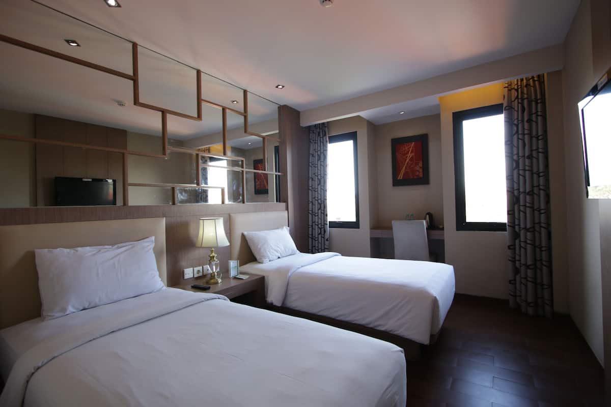 A hotel room with two beds, a desk with a lamp, a TV, and a large window with curtains.