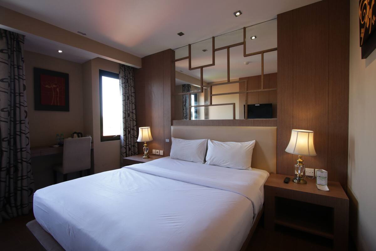 A hotel room with a large bed, two bedside tables with lamps, a desk, and a chair.